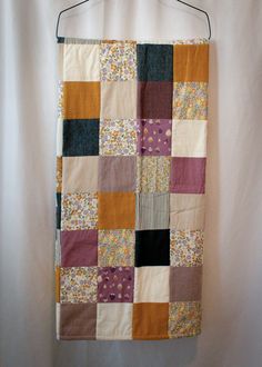 a patchwork quilt hanging on a white wall with clothes pins attached to the hanger