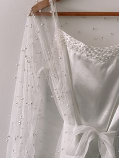 a white dress hanging on a wooden hanger next to a wall with beading