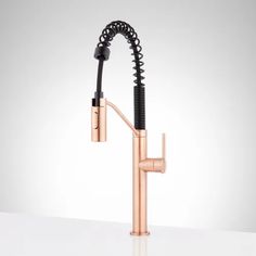 a kitchen faucet with a black hose attached to the side and copper fixtures