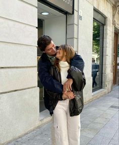 a man and woman kissing on the street in front of a building with an open door