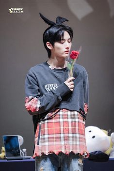 a young man holding a rose in his hand while standing next to a teddy bear