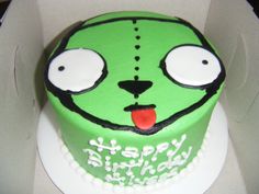 a green cake with white frosting and eyes on it's face in a box