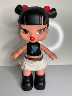 a doll with black hair and red nose is posed on a white surface in front of a wall