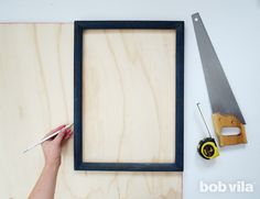 a person holding a pair of scissors next to a wooden frame and plywood board