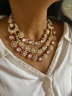 a woman wearing a necklace with pearls and stones on the neck, in front of a white shirt