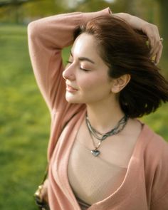 a woman with her hair blowing in the wind, wearing a pink sweater and necklace