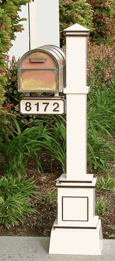 a white mailbox sitting on the side of a road next to bushes and trees