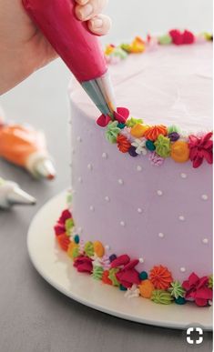 a person is decorating a pink cake with colorful flowers and icing on it