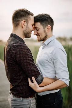 two men standing next to each other with their arms around each other and looking into each others eyes