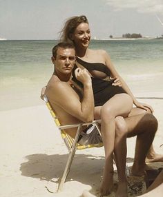 a man and woman are sitting on a beach chair, one is holding the other