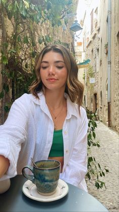 a woman sitting at a table with a cup in front of her and looking down