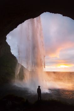 a man standing in front of a waterfall at sunset or sunrise with the sun setting