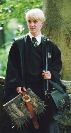 a young boy dressed in harry potter robes and holding a hogwarts book bag