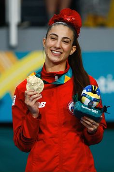 a woman holding a gold medal and wearing a red jacket with her hair in pigtails