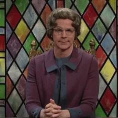 an older woman sitting in front of a stained glass window with her hands folded up