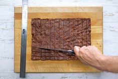 a person cutting into brownies on top of a wooden cutting board