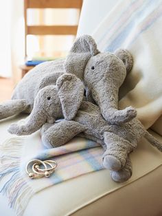 two stuffed elephants laying on top of a couch next to a blanket and pair of scissors