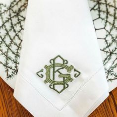 a close up of a white napkin with a green embroidered monogrammed logo on it