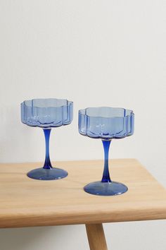 two blue glass dishes sitting on top of a wooden table next to a white wall