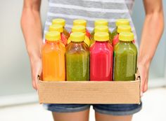 a woman holding a box full of different colored juices and smoothies in it