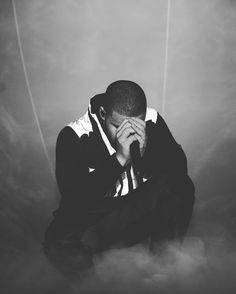 a black and white photo of a man sitting on the ground with his hands to his face