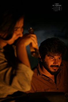 a man and woman sitting next to each other in the dark with one holding a bottle