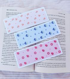 three bookmarks sitting on top of an open book with pink and blue flowers in them