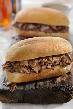 two sandwiches sitting on top of a piece of wood next to each other with meat in between them