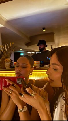 two beautiful women sitting next to each other in front of a bar and one is holding a cell phone