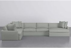 a large sectional couch with pillows on the back and side ends, in front of a white wall