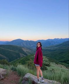 a woman standing on top of a rock with mountains in the background