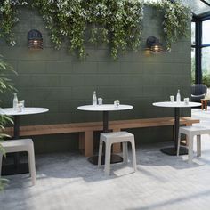 an outdoor seating area with tables and stools in front of a green wall filled with hanging plants