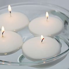 four white candles floating in a glass bowl