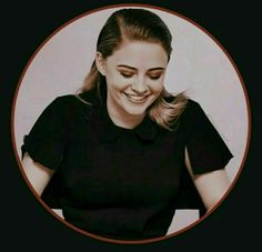 a woman smiling while sitting in front of a white wall