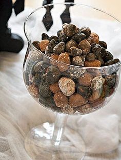 a glass bowl filled with rocks on top of a white cloth covered table next to a black cat