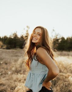 a woman standing in a field smiling at the camera