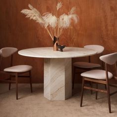 a white marble table with four chairs and a vase filled with dried grass on top