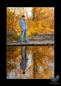 a man standing in front of a body of water with trees reflected in the water