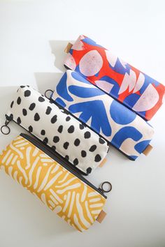 four different colored pencil cases sitting next to each other on a white surface with black dots