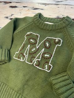 a green sweater with the letters m and l on it is sitting on a wooden surface