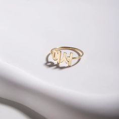 a gold monogrammed ring with two initials on the front and back, sitting on top of a white surface