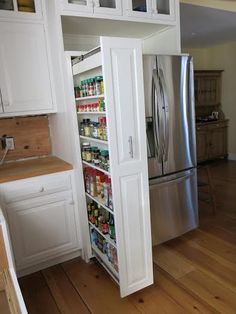 an open pantry in the middle of a kitchen with white cabinets and wood flooring