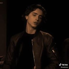 a young man is sitting in a dark room and looking at the camera while wearing a leather jacket