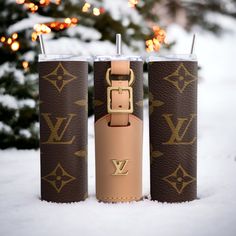 two louis vuitton travel mugs sitting in the snow next to a christmas tree