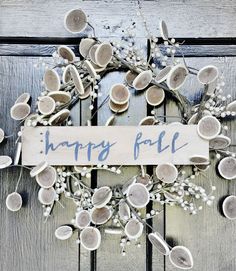 a sign that says happy fall hanging on a wooden door with flowers and leaves around it