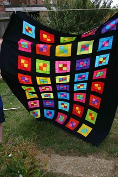 a woman holding up a black quilt with colorful squares on it