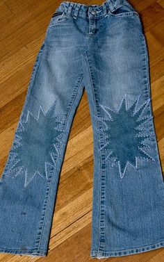 a pair of blue jeans with an embroidered star on the front and back, sitting on a wooden floor