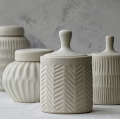 four white vases sitting next to each other on top of a marble countertop