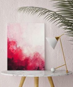 a pink and red painting sitting on top of a table next to a potted plant