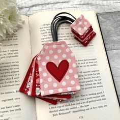 three bookmarks with a heart on them sitting on top of an open book next to a flower